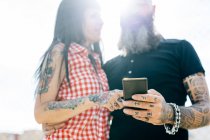 Mature tattooed hipster couple looking at smartphone — Stock Photo