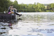 Due ragazze sedute sul molo e guardando nel lago — Foto stock