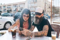 Mature hipster couple looking at smartphone at sidewalk cafe, Valencia, Spain — Stock Photo