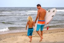 Mature male surfer and son walking toward sea, Asbury Park, New Jersey, USA — Stock Photo