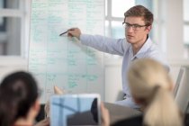 Over the shoulder view of young male office worker giving whiteboard presentation — Stock Photo