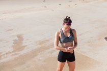 Junge Frau am Strand beim Betrachten von Fitness-Tracker, Carcavelos, Lisboa, Portugal, Europa — Stockfoto