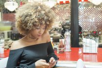 Молода жінка сидить в їдальні і використовує смартфон — стокове фото