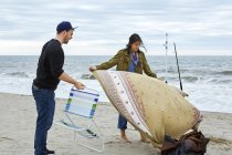 Jeune couple de pêcheurs préparant chaise et couverture de pique-nique sur la plage — Photo de stock