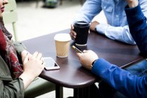 Vista cortada de amigos com smartphones tomando café juntos — Fotografia de Stock