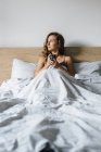 Jovem mulher sentada na cama com xícara de café — Fotografia de Stock