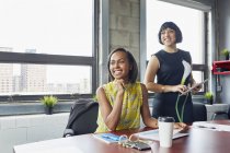 Two women in office looking away and smiling — Stock Photo