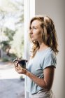 Jeune femme avec café regardant à la porte patio — Photo de stock