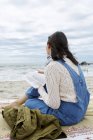 Молодая женщина сидит на пляже и смотрит на море — стоковое фото