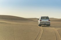 Carro andando pelo deserto entre colinas de areia — Fotografia de Stock