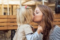 Mãe beijando a filha da criança no banco do parque — Fotografia de Stock
