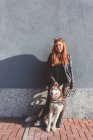 Portrait of red haired woman with dog leaning against wall — Stock Photo