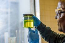Лаборант осматривает стакан желтого биотоплива в лаборатории биотопливного завода — стоковое фото