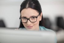 Retrato de jovem trabalhador de escritório do sexo feminino olhando para cima a partir de computador desktop — Fotografia de Stock