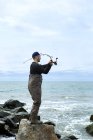 Young man on rock casting fishing rod to sea — Stock Photo