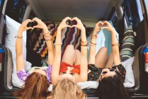Drei junge Frauen liegen auf dem Rücken im Kofferraum und machen Herzenszeichen — Stockfoto