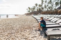 Хлопчик сидить на шезлонгу на пляжі, дивлячись на вигляд — стокове фото