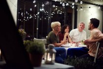 Grupo de pessoas sentadas à mesa, desfrutando de refeição — Fotografia de Stock