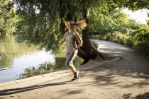 Young female running along park lake path — Stock Photo