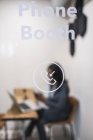 Empresária sentada na cabine telefônica do escritório, usando laptop, segurando smartphone, foco diferencial — Fotografia de Stock