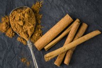 Top view of ground cinnamon and cinnamon sticks on spoon and tabletop — Stock Photo