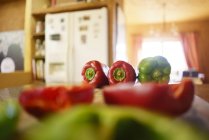 Pimentos vermelhos e verdes inteiros e metades no balcão da cozinha — Fotografia de Stock