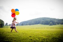 Menina andando no campo rural com um monte de balões coloridos — Fotografia de Stock