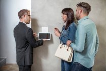 Immobilienmakler steht mit Paar und demonstriert mit digitalem Tablet Technologie im neuen Zuhause — Stockfoto