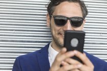 Young businessman in sunglasses looking at smartphone — Stock Photo