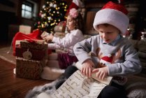 Young girl and boy sorting Christmas gifts, young boy rolling list — Stock Photo