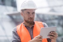 Man in hard hat and high visibility jacket using digital tablet — Stock Photo