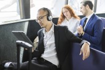 Бизнесмен в наушниках смотрит на цифровой планшет на пассажирском пароме — стоковое фото