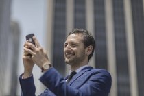 Smiling young businessman taking selfie outside office building — Stock Photo