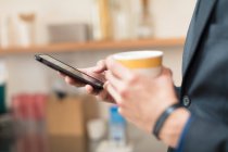 Руки бізнесмена, що тримає чашку кави та смартфон — стокове фото