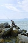 Joven pescador de mar macho pisando rocas de playa - foto de stock