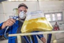 Homme peinture par pulvérisation pièce de voiture dans l'atelier de réparation de carrosserie — Photo de stock