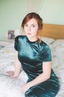 Portrait of young woman in shiny green dress sitting on bed — Stock Photo