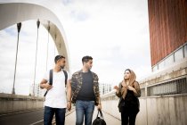 Three friends walking across urban bridge — Stock Photo