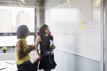 Two women in office using whiteboard and sticky notes — Stock Photo