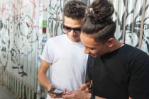 Dos jóvenes significan en la calle, mirando el teléfono inteligente - foto de stock