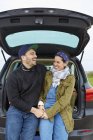 Giovane coppia seduta e ridendo nel bagagliaio auto aperta — Foto stock