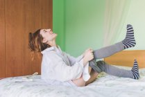 Laughing young woman on bed putting on leggings — Stock Photo