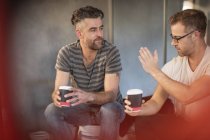 Dos hombres tomando un descanso con tazas de café y discutiendo - foto de stock