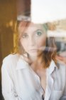 Portrait of beautiful young woman looking through window — Stock Photo