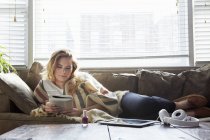 Giovane donna che legge libro sul divano — Foto stock