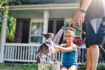 Батько і дочка миють собаку з шлангом — стокове фото