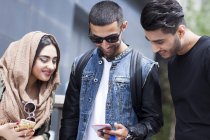 Трое друзей на улице смотрят на смартфон — стоковое фото