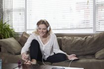 Donna che dipinge unghie e ascolta musica sul divano — Foto stock