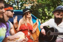 Young adult friends playing acoustic guitar while festival camping — Stock Photo