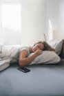 Jeune femme endormie avec smartphone sur le lit — Photo de stock
